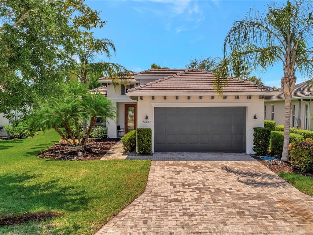 A single-story house with a gray garage door, tile roof, and a paved driveway — 5009 LAKE OVERLOOK AVENUE, BRADENTON, FL