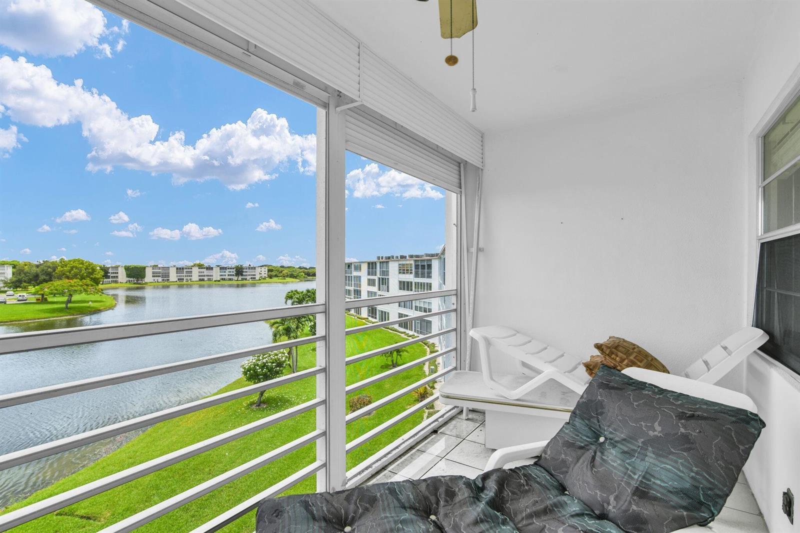 A screened-in balcony overlooks a lake and apartment buildings with white lounge chairs inside — 4053 Wolverton C, Boca Raton FL 33434, BOCA RATON, FL