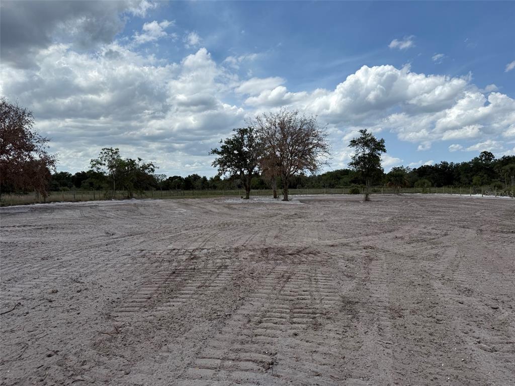 A wide, cleared dirt lot features scattered trees under a cloudy blue sky — 14667 NW 310TH STREET, OKEECHOBEE, FL