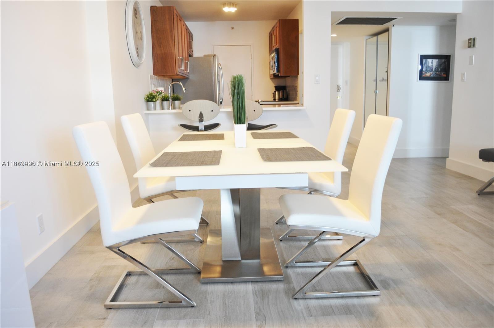 A dining room features a white table with four modern chairs and a kitchen backdrop — 100 Lincoln Rd # 435, Miami Beach FL 33139, MIAMI BEACH, FL