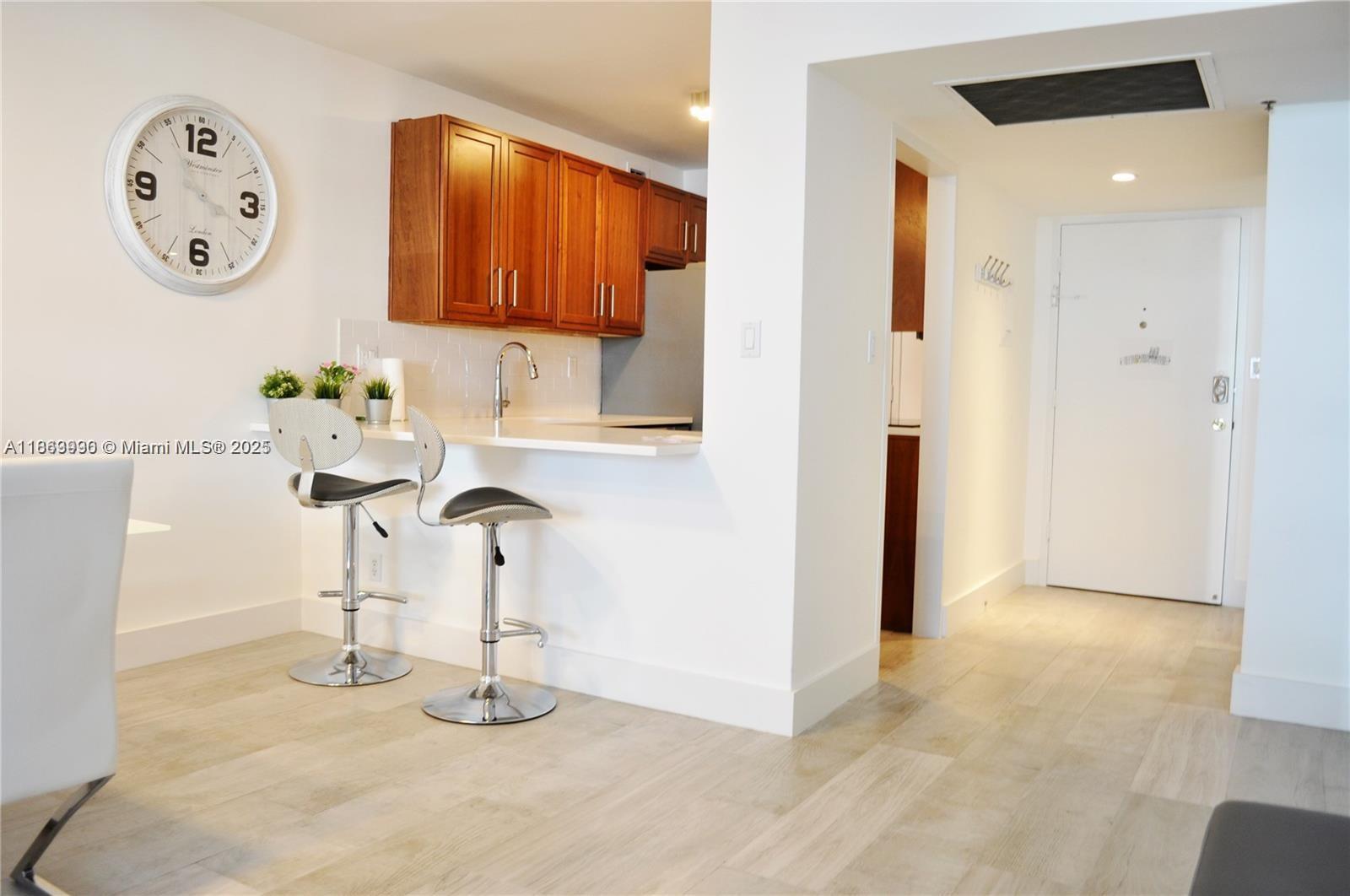 A kitchen with wood cabinets and a breakfast bar sits next to an entryway — 100 Lincoln Rd # 435, Miami Beach FL 33139, MIAMI BEACH, FL