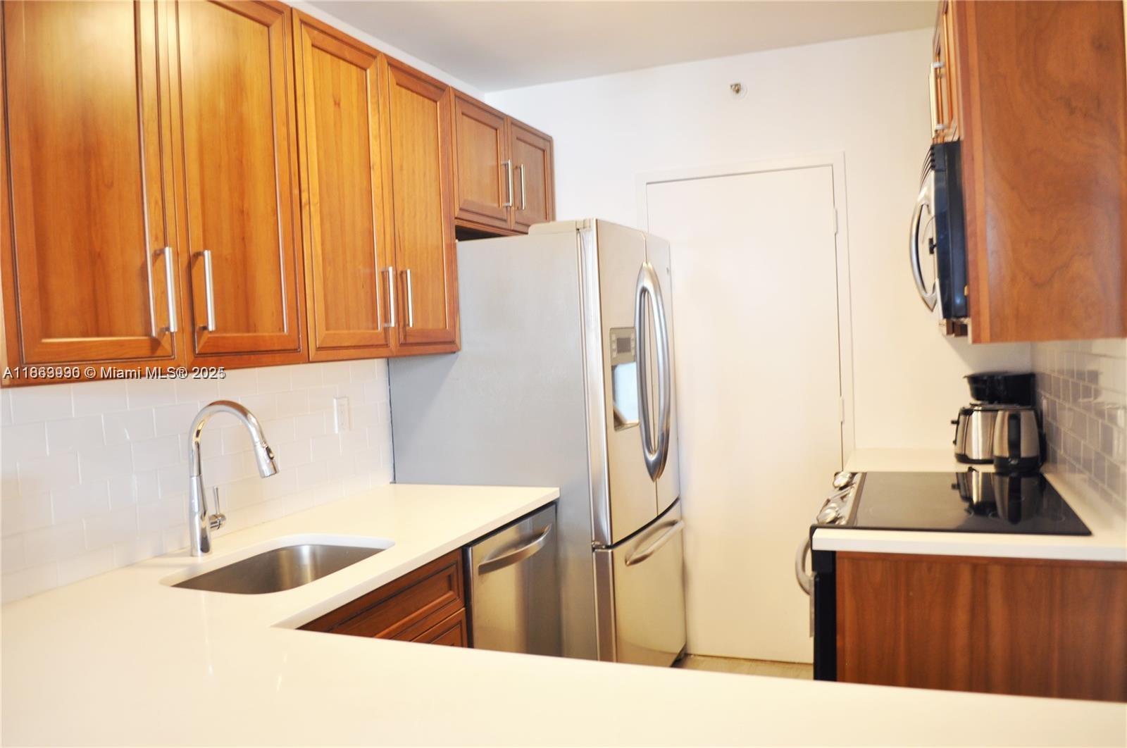 A kitchen features wood cabinets, stainless steel appliances, white countertops, and a subway tile backsplash — 100 Lincoln Rd # 435, Miami Beach FL 33139, MIAMI BEACH, FL
