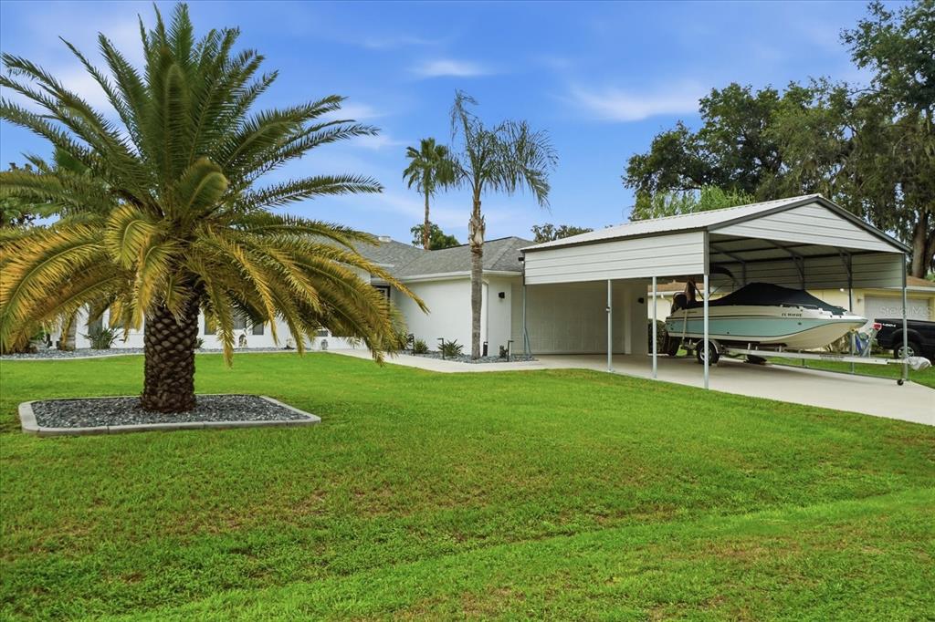 A white house with a large palm tree and a metal carport housing a boat — 4457 E AVOCET COURT, INVERNESS, FL