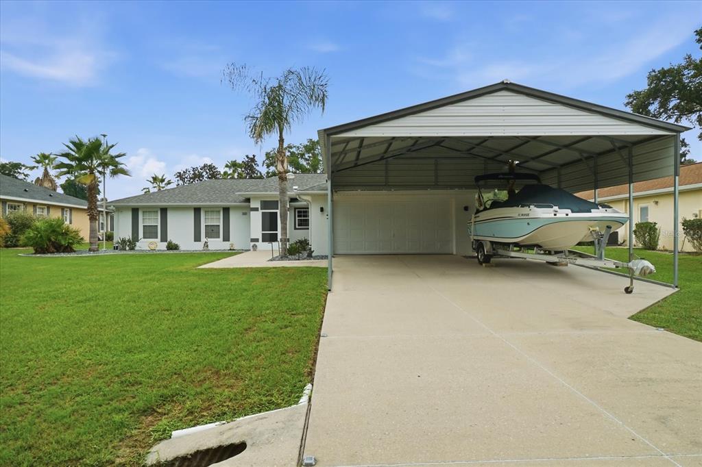 A single-story house features a large metal carport sheltering a boat on a concrete driveway — 4457 E AVOCET COURT, INVERNESS, FL