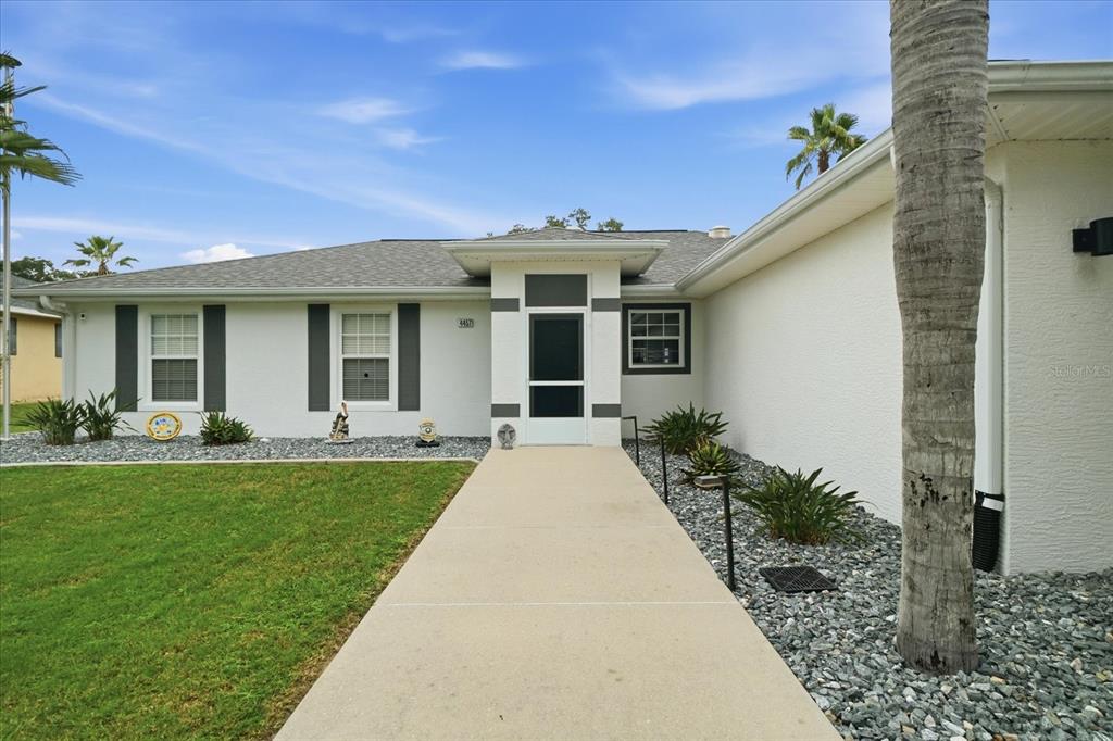 A concrete walkway leads to the front entrance of a single-story house with gray shutters — 4457 E AVOCET COURT, INVERNESS, FL