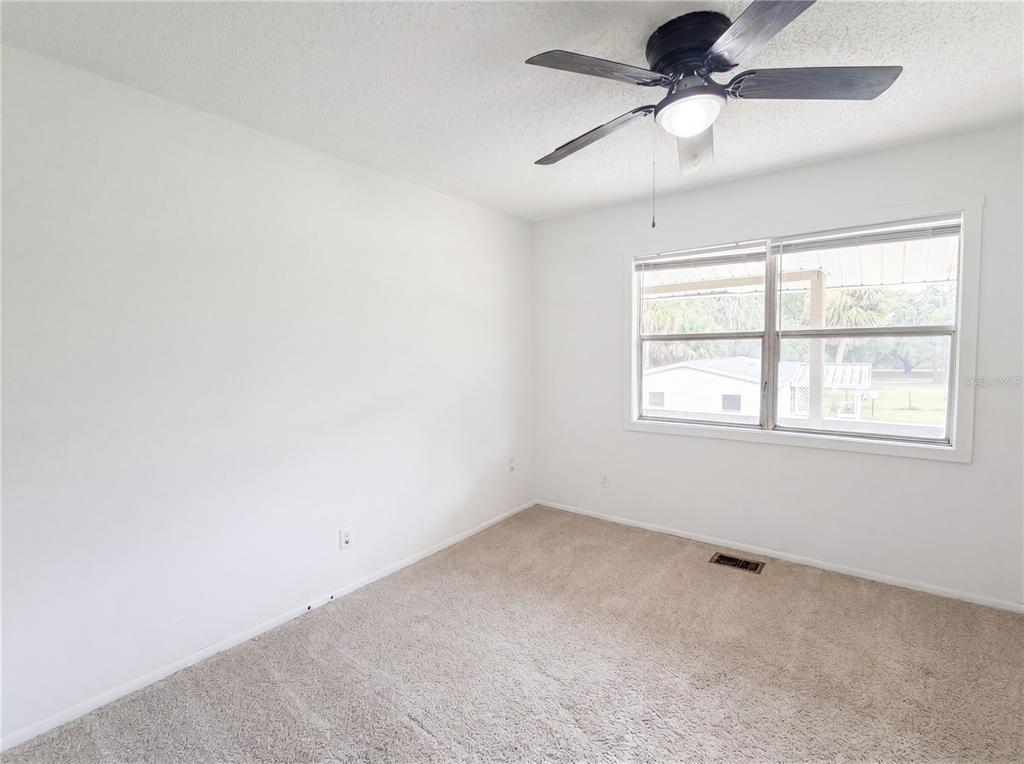 An empty bedroom features white walls, beige carpeting, a ceiling fan, and a window — 22415 HORIZON VISTAS DRIVE, EUSTIS, FL