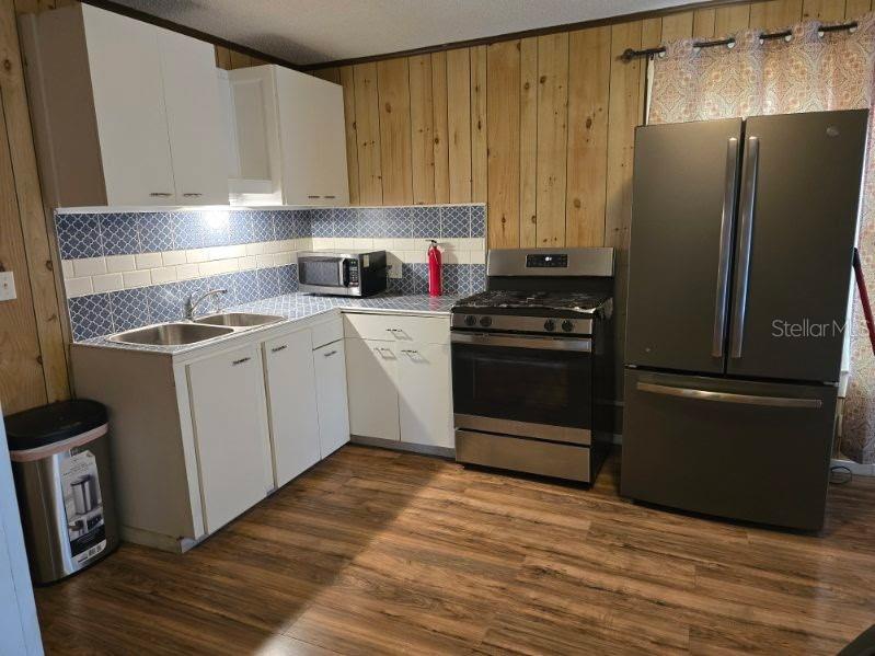 A kitchen features white cabinets, wood-paneled walls, stainless steel appliances, and blue patterned backsplash tiles — 1611 INDIAN TRAIL, LEESBURG, FL