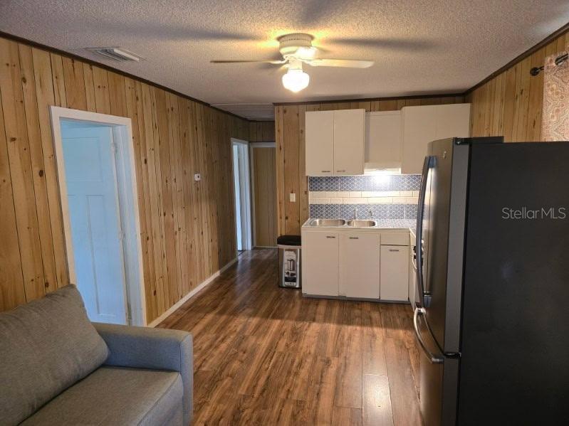A kitchen and living area featuring wood-paneled walls, wood-look flooring, and white cabinetry — 1611 INDIAN TRAIL, LEESBURG, FL