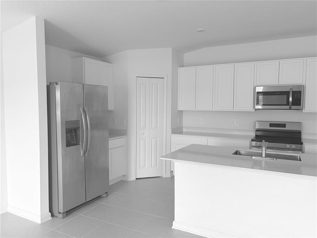 A kitchen features white cabinetry, stainless steel appliances, and a central island with a sink — 2934 PENNACHIO DRIVE, LAKE WALES, FL