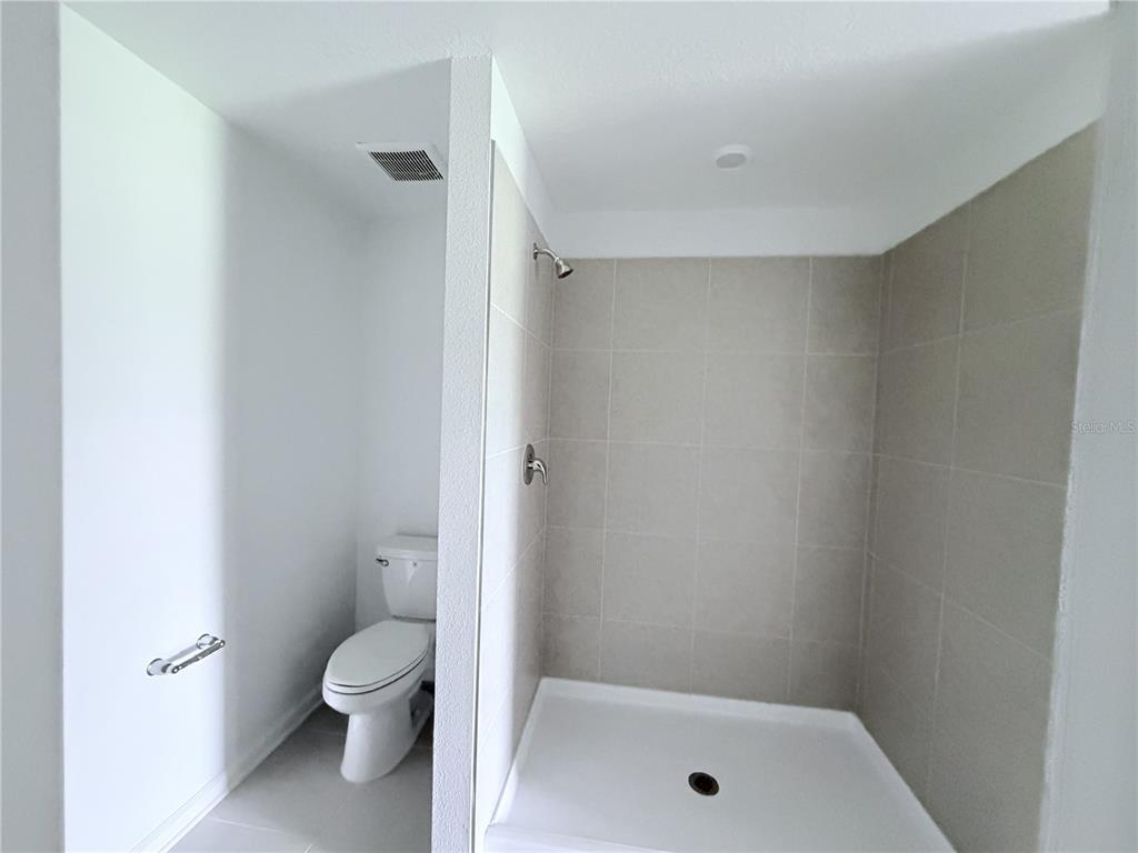 A bathroom features a walk-in shower with beige tile walls next to a white toilet — 2934 PENNACHIO DRIVE, LAKE WALES, FL