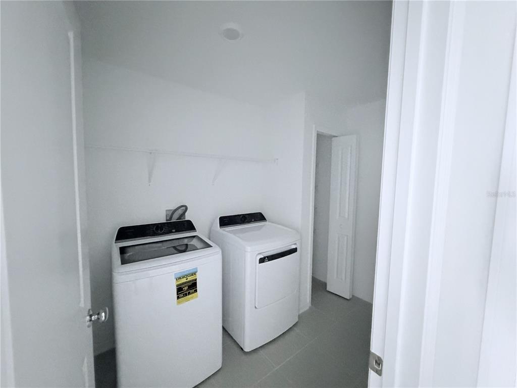 A laundry room features white walls, tile flooring, a shelf, and a washer and dryer — 2934 PENNACHIO DRIVE, LAKE WALES, FL