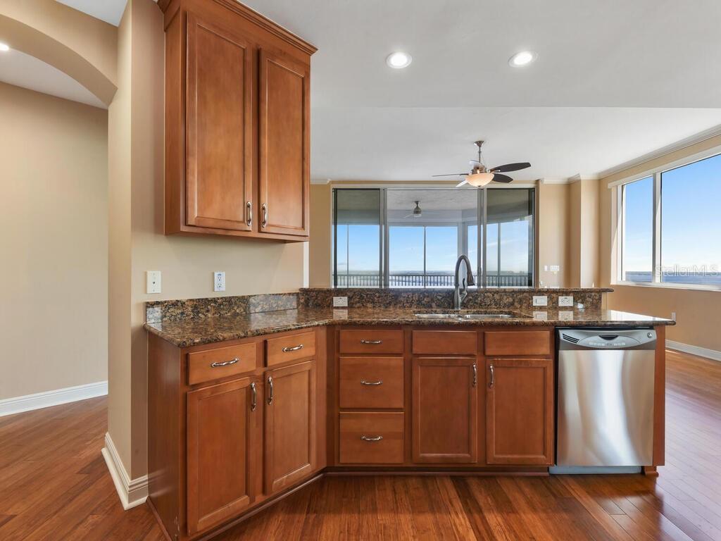 A kitchen with wood cabinets, granite countertops, and a stainless steel dishwasher overlooks a balcony — 2104 W FIRST STREET UNIT 2304, FORT MYERS, FL