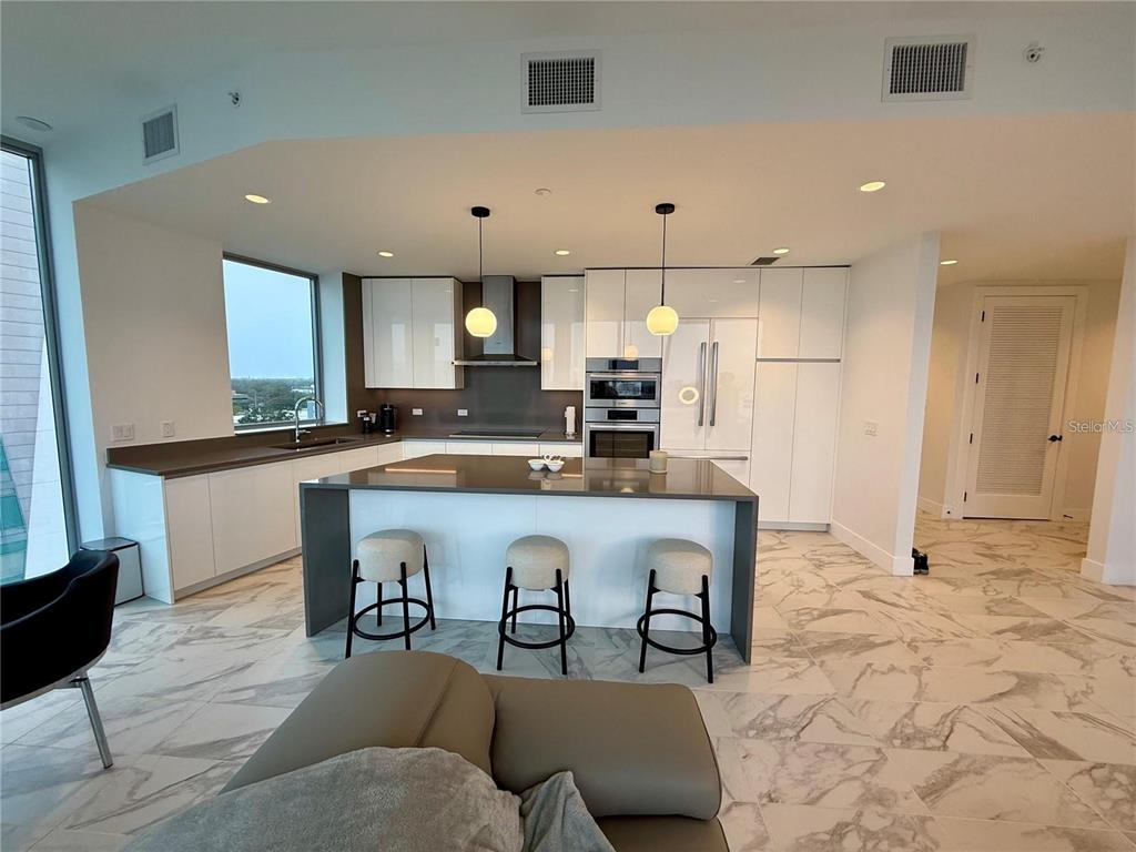 A modern kitchen features white cabinetry, a large gray island with three stools, and marble flooring — 777 3RD AVENUE N UNIT 908, ST PETERSBURG, FL