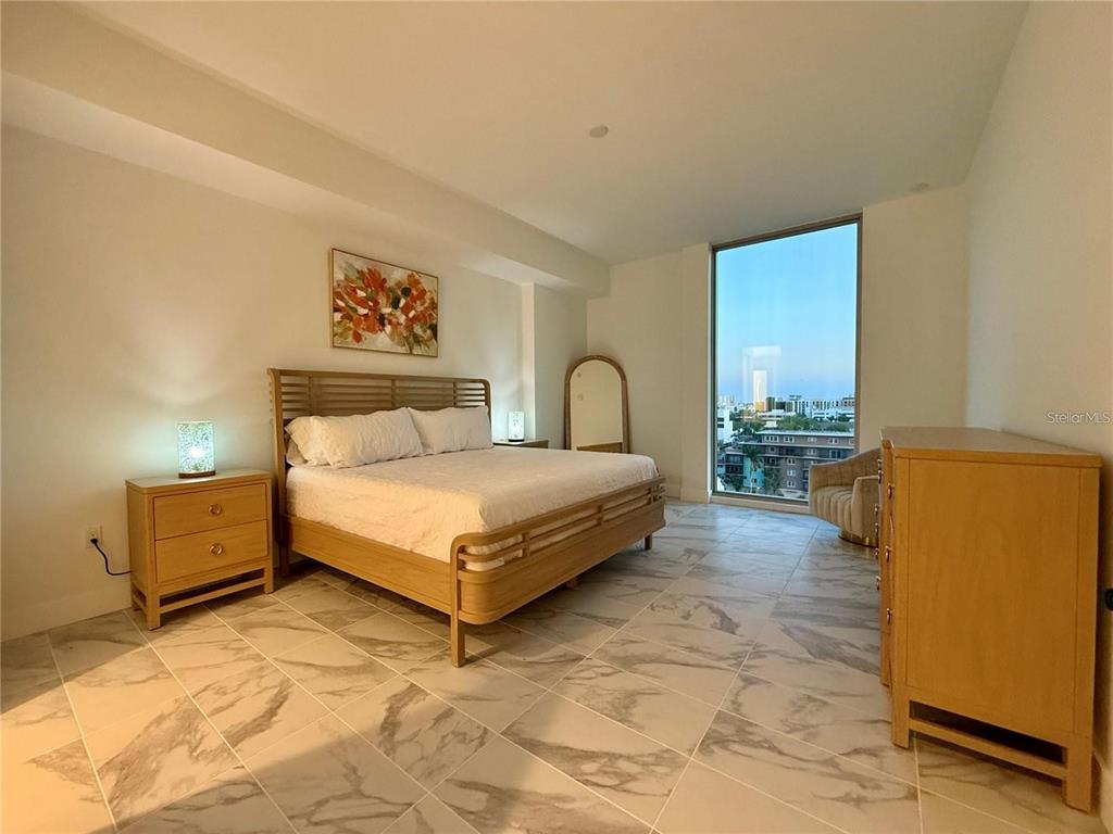A bedroom features a wooden bed frame, marble-look tile flooring, and a floor-to-ceiling window — 777 3RD AVENUE N UNIT 908, ST PETERSBURG, FL