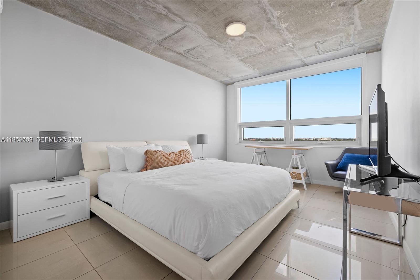 A bedroom features a white bed, concrete ceiling, tile floors, and large windows — 3250 NE 1st Ave # 1113, Miami FL 33137, MIAMI, FL
