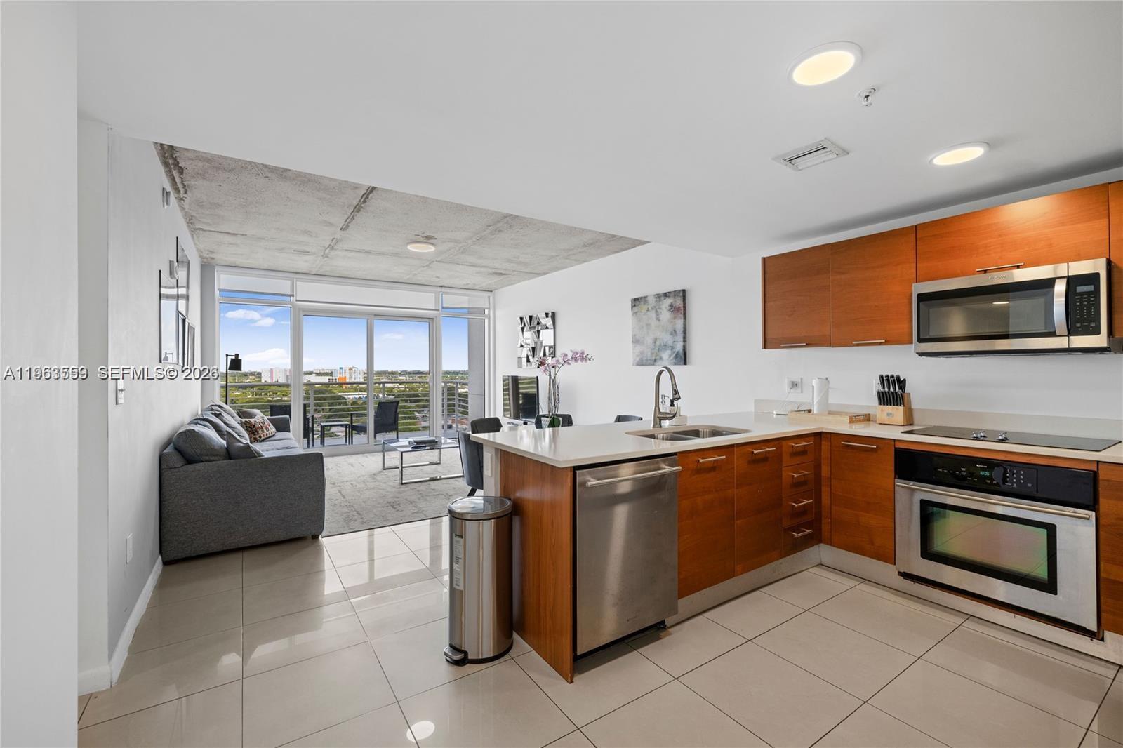 A modern kitchen with wood cabinets and stainless steel appliances opens to a living area — 3250 NE 1st Ave # 1113, Miami FL 33137, MIAMI, FL