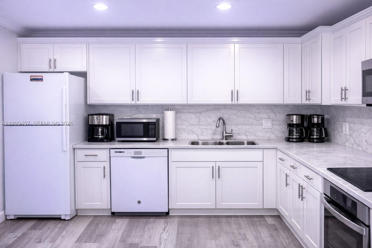 A kitchen features white cabinets, stainless steel appliances, and a marble-patterned countertop and backsplash — 2420 SW 81st Ave # 403, Davie FL 33324, DAVIE, FL
