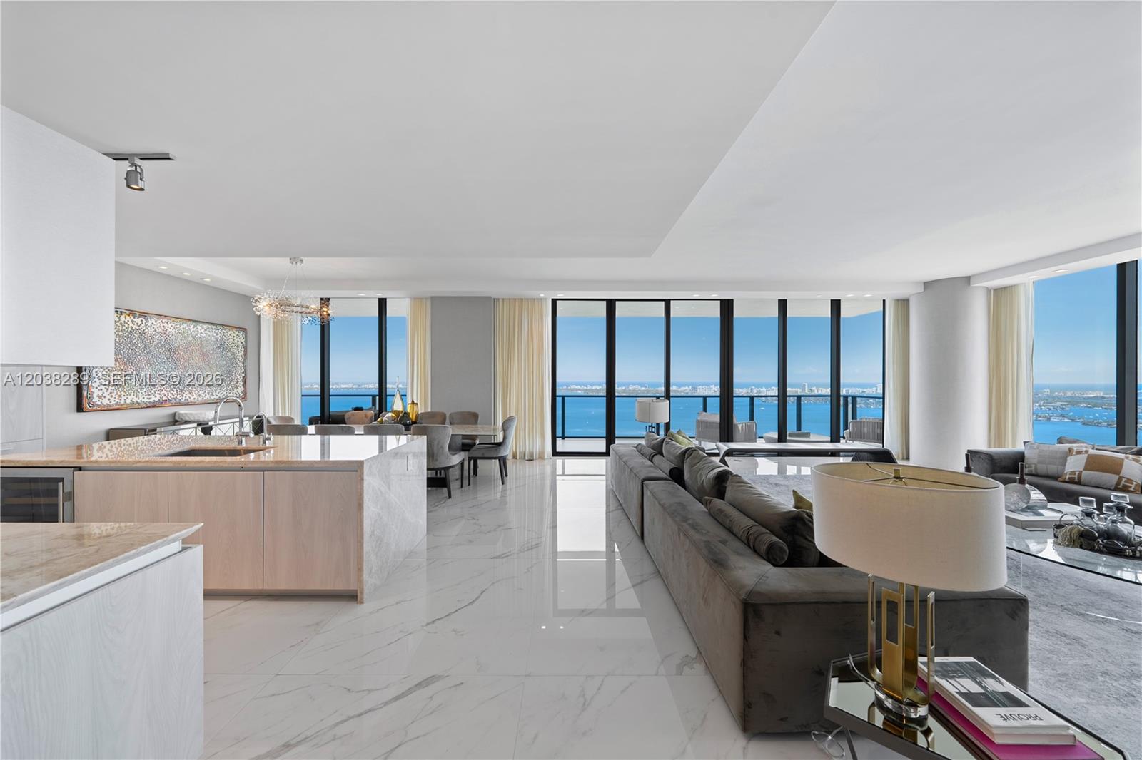 A modern open-concept living and dining area features marble floors, a kitchen island, and ocean views — 3131 NE 7th Ave, Miami FL 33137, MIAMI, FL