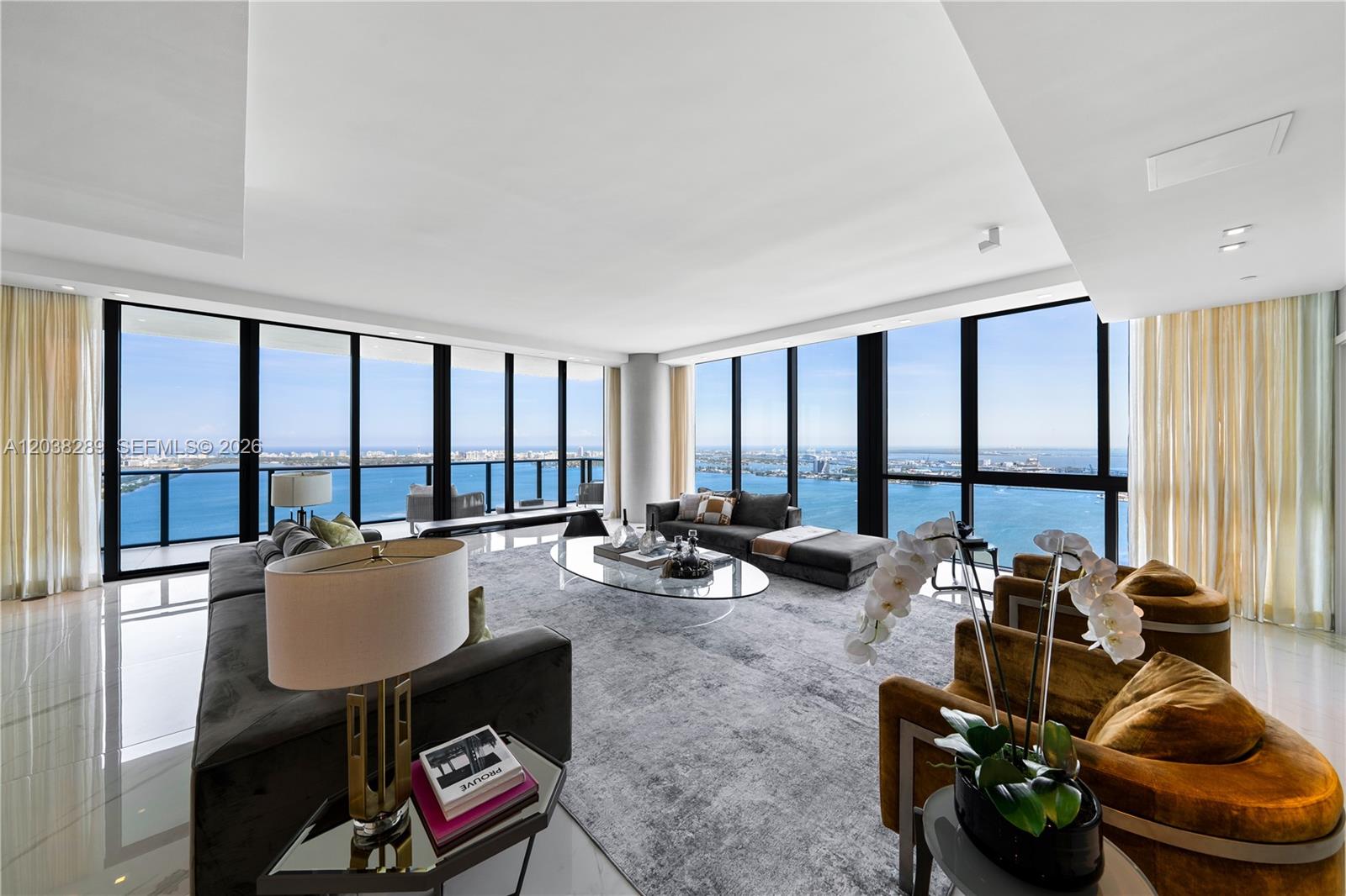 A modern living room features floor-to-ceiling windows with panoramic ocean views and tiled flooring — 3131 NE 7th Ave, Miami FL 33137, MIAMI, FL