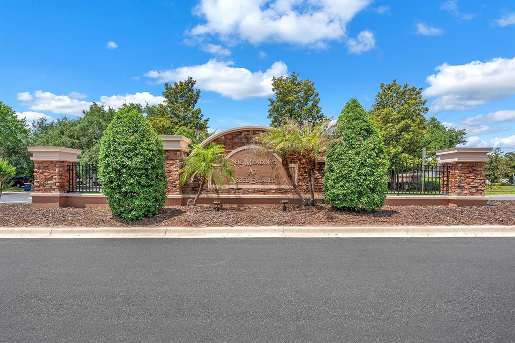 A stone entrance sign for The Meadows at Asbel Estates stands behind a paved road — 9625 BATON ROUGE LANE, LAND O LAKES, FL