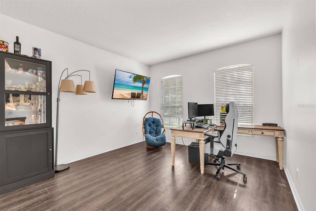 A home office features dark wood flooring, a desk with a computer, and a wall-mounted television — 9625 BATON ROUGE LANE, LAND O LAKES, FL