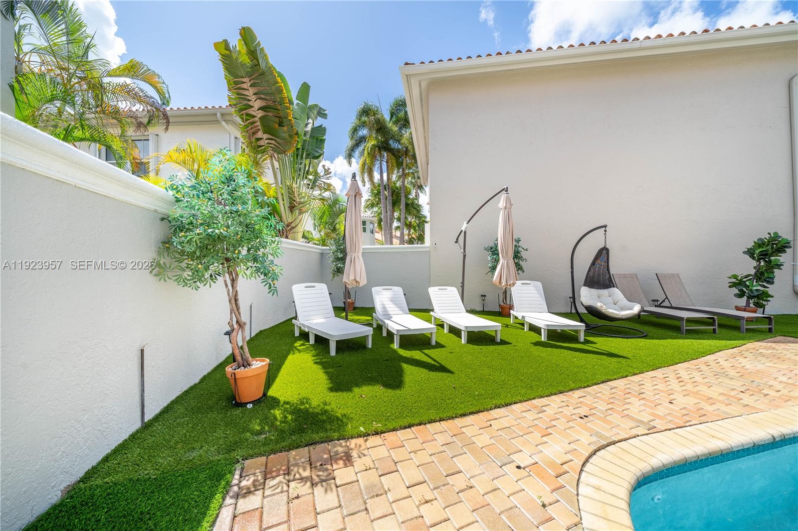 A backyard patio features artificial turf, four lounge chairs, a hanging chair, and a pool — 1547 Mariner Way, Hollywood FL 33019, HOLLYWOOD, FL