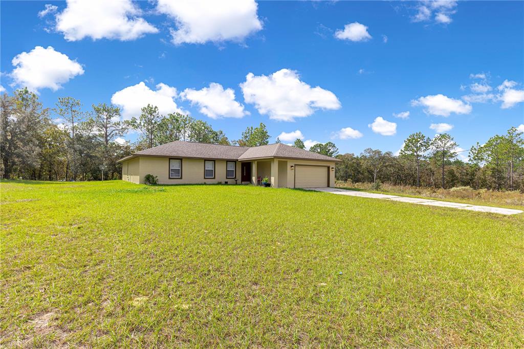A single-story house with a tan exterior, a two-car garage, and a large grassy yard — 12182 SW 91ST LANE, DUNNELLON, FL