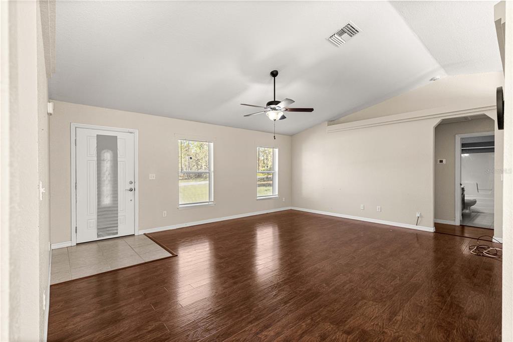 A spacious living room features vaulted ceilings, wood-look flooring, and a front entry door — 12182 SW 91ST LANE, DUNNELLON, FL