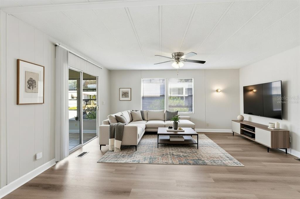 A living room features light wood-look flooring, a sectional sofa, a rug, and a television — 29250 US HIGHWAY 19 N UNIT 578, CLEARWATER, FL
