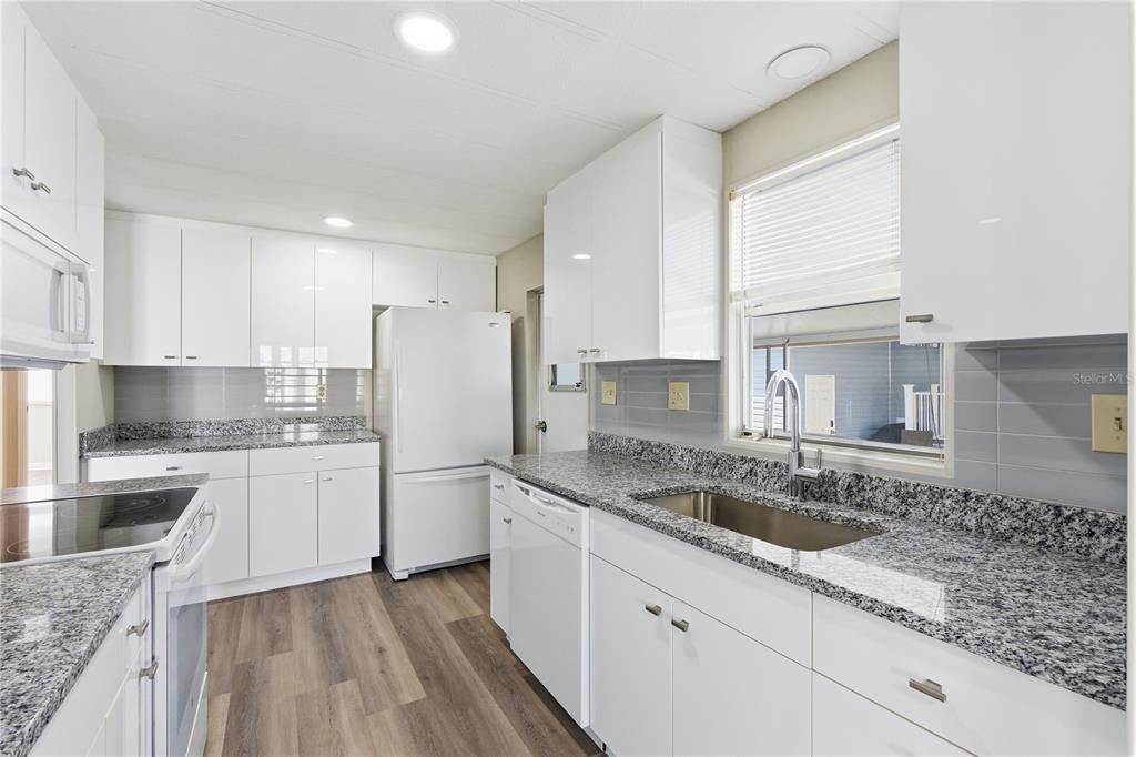 A kitchen features white cabinets, granite countertops, a stainless steel sink, and wood-look flooring — 29250 US HIGHWAY 19 N UNIT 578, CLEARWATER, FL