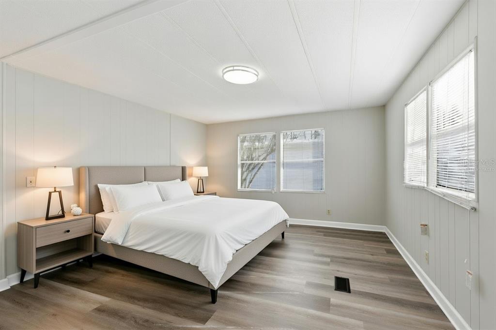 A bedroom features a bed with a gray headboard, wood-look flooring, and white paneled walls — 29250 US HIGHWAY 19 N UNIT 578, CLEARWATER, FL