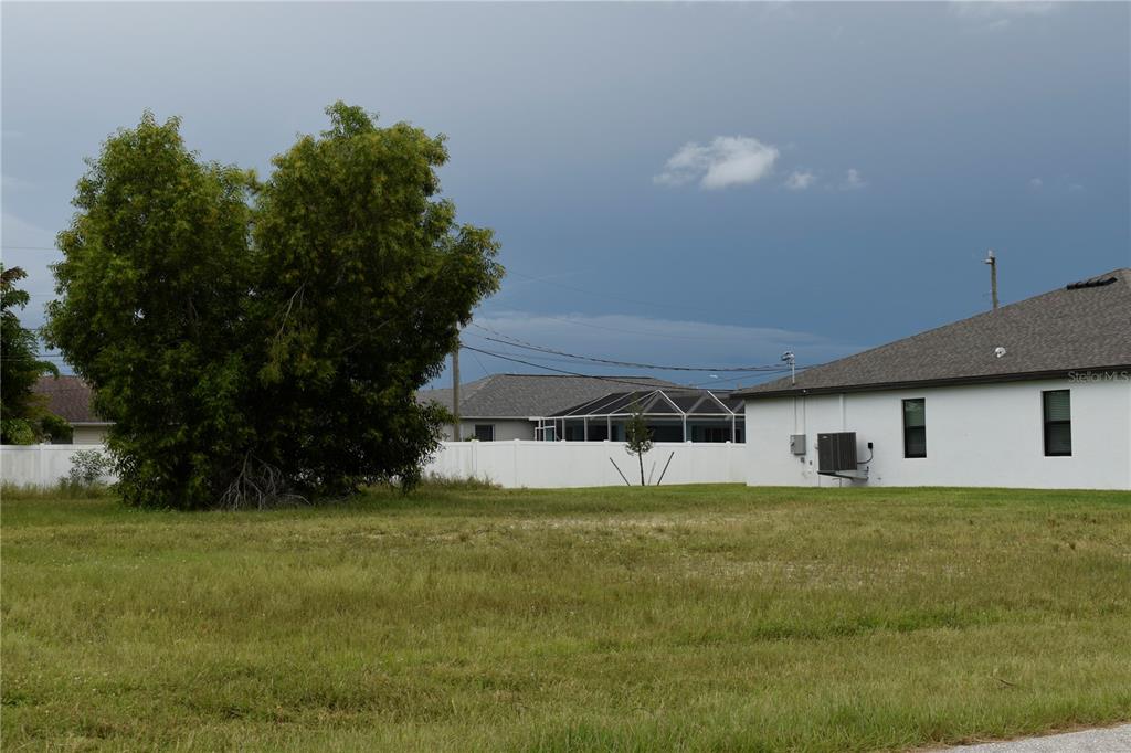 A grassy vacant lot sits in front of a white fence and a residential house — 706 SW 21 STREET, CAPE CORAL, FL