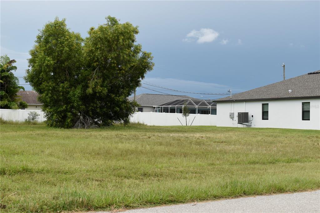 A grassy vacant lot sits next to a white house with a white fence — 706 SW 21 STREET, CAPE CORAL, FL