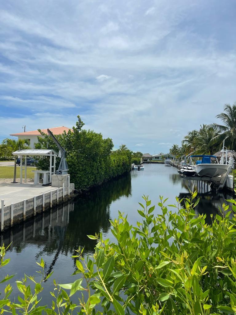 A canal view featuring a boat lift, a concrete dock, and lush green vegetation — 30351 Flamingo Ln, Big Pine FL 33043, BIG PINE, FL