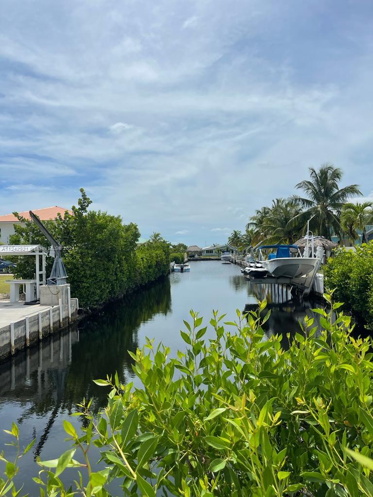 A canal view features a boat lift, lush greenery, and residential properties under a cloudy sky — 30351 Flamingo Ln, Big Pine FL 33043, BIG PINE, FL