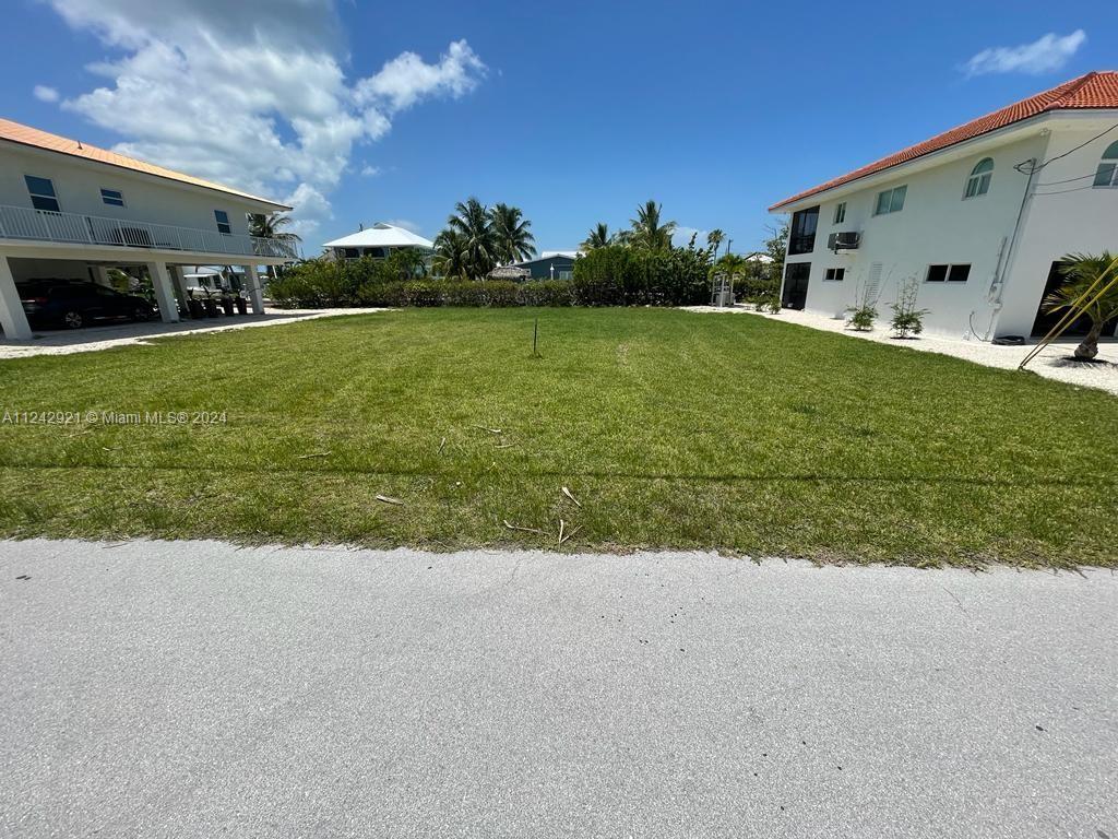 A grassy vacant lot sits between two white multi-story houses under a blue sky — 30351 Flamingo Ln, Big Pine FL 33043, BIG PINE, FL