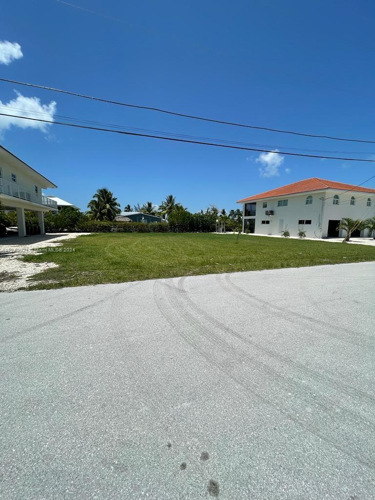 A vacant grassy lot sits between two white multi-story houses under a clear blue sky — 30351 Flamingo Ln, Big Pine FL 33043, BIG PINE, FL