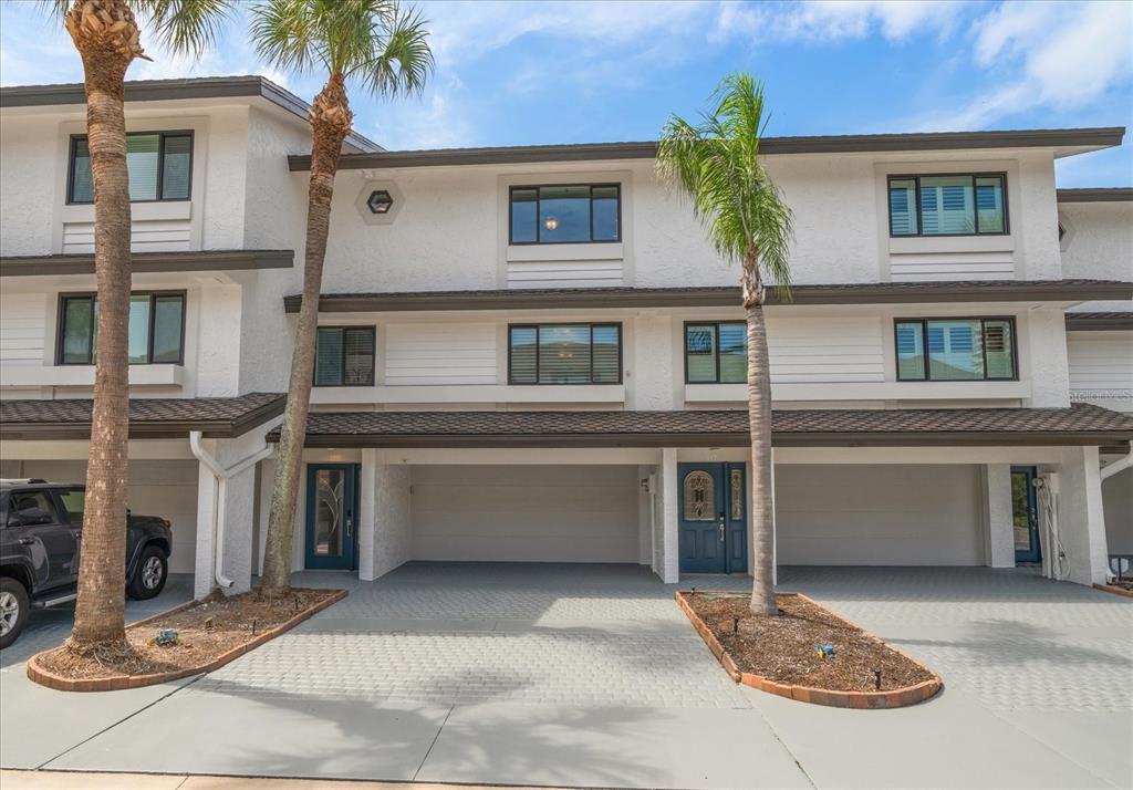 The exterior of a multi-story townhouse features a covered carport, palm trees, and paved driveway — 119 MARINA DEL REY COURT, CLEARWATER BEACH, FL