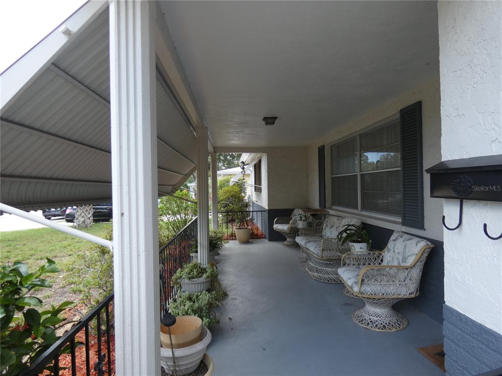 A covered front porch features wicker furniture, potted plants, and a metal awning — 5248 IRONWOOD LANE, NEW PORT RICHEY, FL