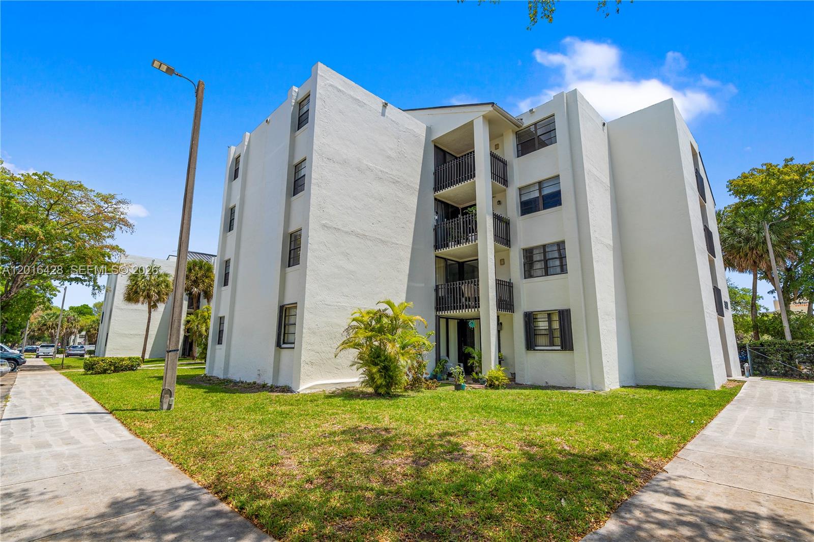 A three-story white apartment building features balconies and a lawn under a blue sky — 3561 SW 117th Ave # 206, Miami FL 33175, MIAMI, FL
