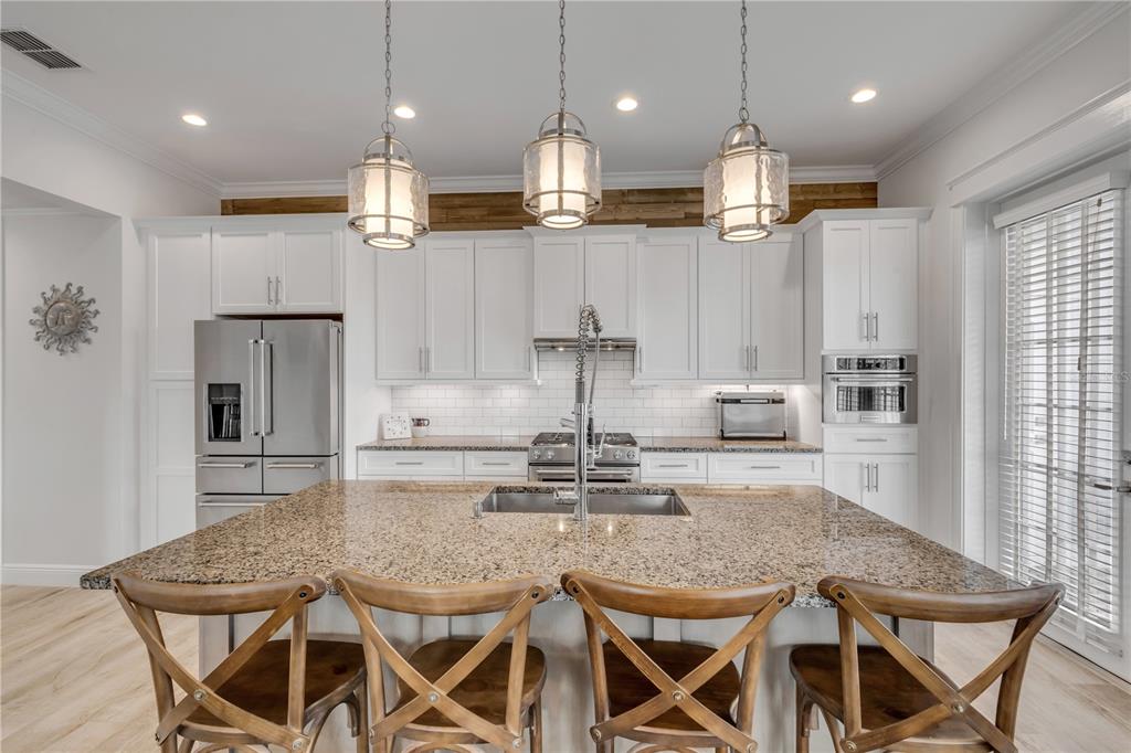 A kitchen features white cabinetry, a granite-topped island with four wooden chairs, and pendant lighting — 4636 SAXON DRIVE, NEW SMYRNA BEACH, FL