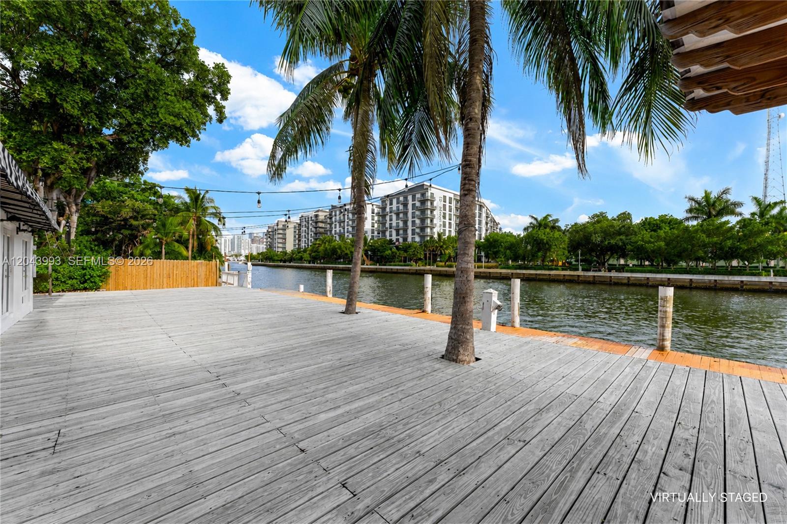 A large wooden deck overlooks a canal with palm trees and apartment buildings in view — 1110 NW North River Dr, Miami FL 33136, MIAMI, FL