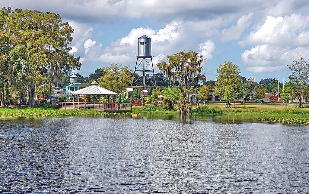 A water tower stands behind a gazebo and playground near a lake with trees — 2907 CLEARWOOD STREET, INVERNESS, FL