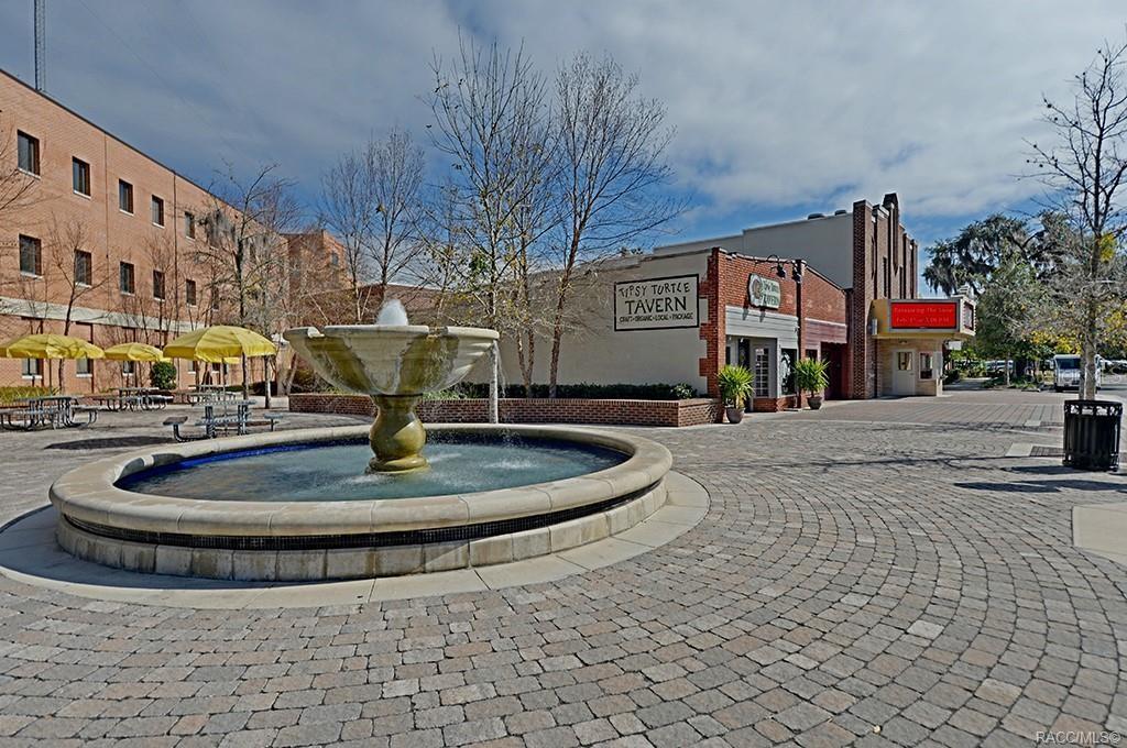 A stone fountain sits in a paved plaza in front of a brick tavern building — 2907 CLEARWOOD STREET, INVERNESS, FL