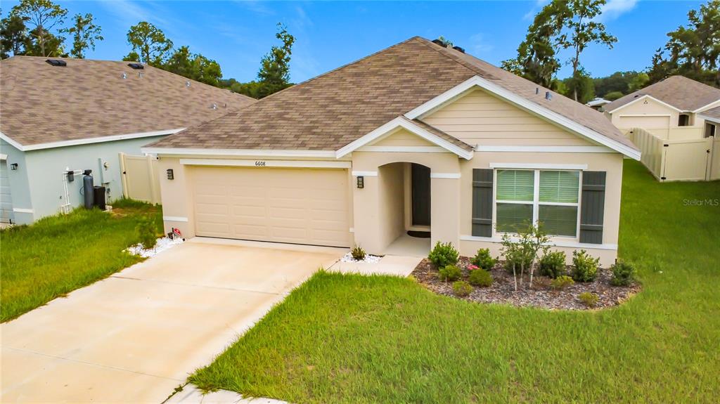 A single-story suburban house with a tan stucco exterior, a two-car garage, and a lawn — 6608 SE 1ST LOOP, OCALA, FL