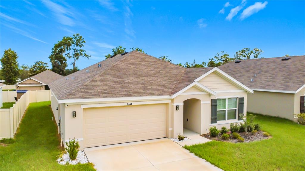 A single-story suburban house features a tan stucco exterior, a two-car garage, and a driveway — 6608 SE 1ST LOOP, OCALA, FL