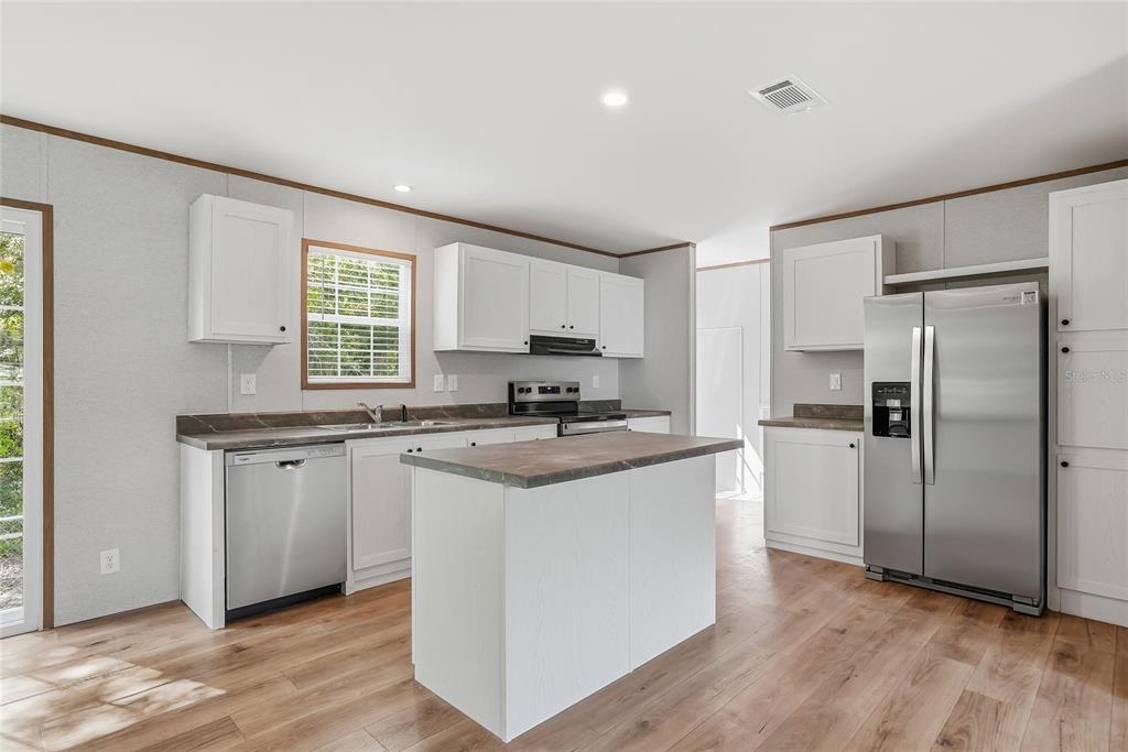A kitchen features white cabinets, stainless steel appliances, a center island, and wood-look flooring — 12015 WESTBAY AVENUE, NEW PORT RICHEY, FL