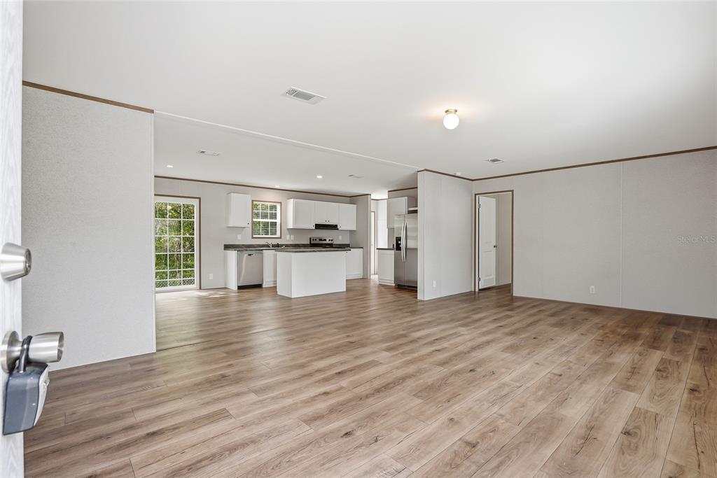 An open-concept living area features light wood-look flooring, white walls, and a kitchen with white cabinets — 12015 WESTBAY AVENUE, NEW PORT RICHEY, FL
