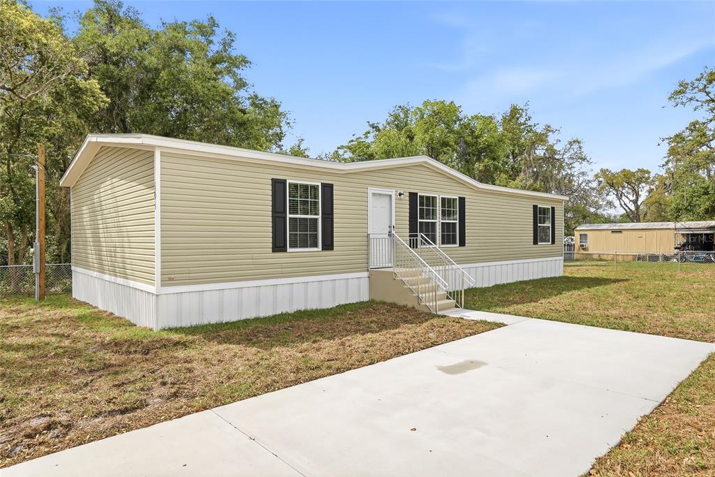 A tan manufactured home with black shutters sits on a lot with a concrete driveway — 12015 WESTBAY AVENUE, NEW PORT RICHEY, FL