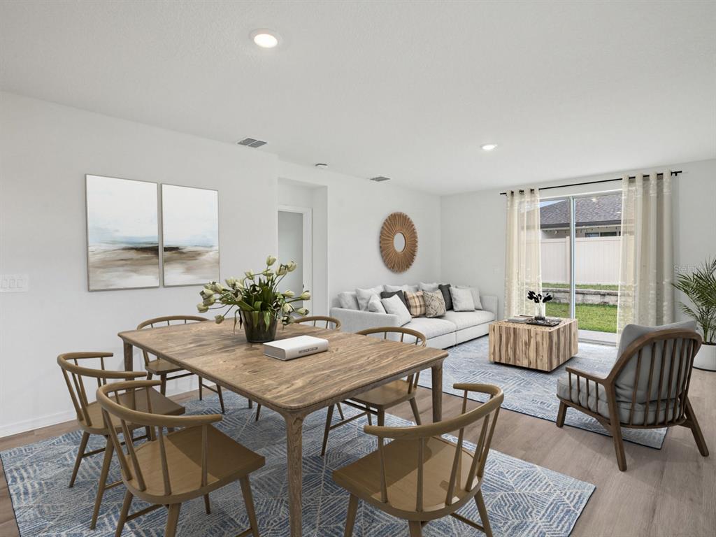 A dining area and living room with light wood floors, neutral furniture, and sliding glass doors — 3744 MOSCATO DRIVE, BROOKSVILLE, FL